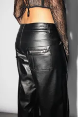 Pantalón recto de cuerina color negro, tiro medio-bajo con recortes en el delantero. Acceso mediante cartera de cierre metálico. Cintura con presillas y botón zamak personalizado Top White. Todos sus bolsillos con cierres metálicos. Dos tiras decorativas con botón snap en piernas delanteras. Detalle de avío pasador marcario en trasero.