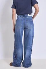 Pantalón de jean azul con bordados florales y aberturas en forma de flor en las piernas.