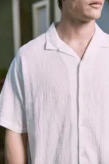 Camisa blanca de popelina con cuello resort, mangas cortas y cierre frontal con botones.