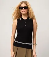 Top de punto sin mangas color negro, ajustado al cuerpo, con cuello polo que presenta ribetes blancos contrastantes. Tiene un cierre frontal de tres botones y un ribete blanco en el ruedo inferior.