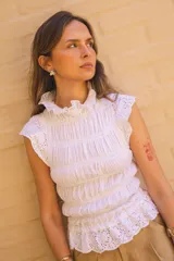 Blusa blanca de algodón con textura fruncida y detalles de broderie en cuello, mangas y ruedo.