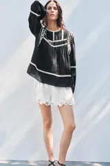 Blusa negra de algodón con cuello redondo y manga larga abullonada. Presenta bordados blancos a contraste en el cuello, hombros y mangas. Cierre en la espalda con abertura y botón.