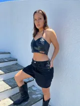 Top negro de cuero sintético, corte crop, con breteles finos regulables y etiqueta con logo de la marca en el frente.