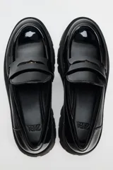 Zapato tipo mocasín negro acharolado con antifaz y suela track.