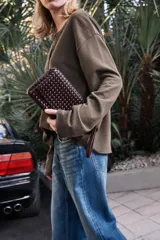 Bolso alargado color borgoña con diseño trenzado, asa bandolera y tirador con pulsera de mano. Incluye bolsillo interior, cierre mediante solapa y botón imantado.