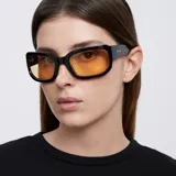 Lentes de sol negros con forma rectangular envolvente y lentes amarillas.