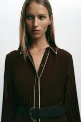 Vestido midi marrón chocolate plisado, con cuello solapa, manga larga y cinturón. Presenta cierre frontal con botones y vivos blancos a contraste en cuello, mangas y botonera. Incluye forro interior.