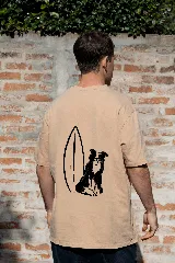 Remera color arena de manga corta con estampa en la espalda de un perro sentado junto a una tabla de surf.