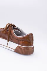 Zapatillas bajas color marrón con textura simil cuero de cocodrilo, cordones al tono y suela de goma blanca con detalle marrón.