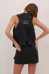 Chaleco negro de denim con proceso de encuerado, tres botones y dos bolsillos grandes laterales.