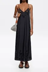 Vestido midi negro de corte recto y fluido, con escote pico pronunciado y tirantes finos. Presenta bordado inglés con motivos florales en el escote, laterales y ruedo.