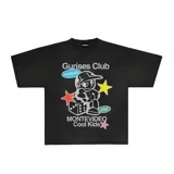 Remera negra de corte boxy con estampa de un personaje de historieta con gorra, dados y estrellas. Incluye texto "Gurises Club", "Uruguay", "Montevideo Cool Kids" y el logo de la marca Kaboa.