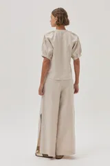 Blusa de lino color arena, de manga corta, con cuello redondo y lazo ajustable. Presenta bordados en las mangas y el escote.