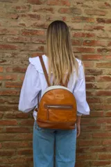Mochila pequeña de cuero color camel, con base marrón, laterales color crema y cierre superior con cremallera.