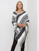 Poncho de tejido suave con diseño de rayas anchas en tonos blanco, gris claro, gris oscuro y negro. Tiene cuello en V cruzado y terminación con flecos en el ruedo.