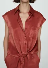 Camisa color ladrillo de tejido satinado, con cuello camisero, mangas cortas, bolsillo de parche en el pecho y cierre frontal con botones.