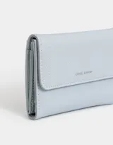 Billetera celeste de cuerina granulada con solapa y tag de metal. Cuenta con broche con botón para cerrado y compartimentos para tarjetas y billetes.