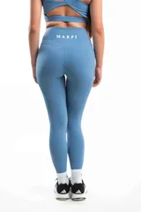 Conjunto deportivo color celeste compuesto por top asimétrico de un hombro con logo y calza larga con cintura alta y bolsillos laterales.
