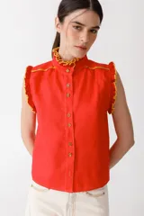 Blusa color mostaza sin mangas, con cuello alto y detalle de volados rojos en cuello, sisas y ruedo. Cierre frontal con botones.