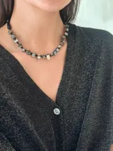 Collar corto con cuentas de nácar con subtono negro, mostacillas y cristales checos. Se cierra con cadena de acero quirúrgico y ganchito para regular el largo.