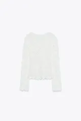 Top blanco de encaje con bordados florales, cuello redondo y mangas largas.