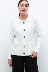 Cardigan crudo de tejido de punto trenzado, con cuello polo, cierre frontal con botones y bolsillos delanteros.