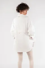 Camisa blanca oversize de nailon arrugado, con cuello clásico, cierre frontal con botones, manga larga raglán, puños abotonados, bolsillo utilitario en el pecho, bolsillos laterales y canesú abotonado en la espalda.