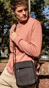 Morral de tela canvas color verde oliva, con tapa, apertura superior y cierre. Tiene bolsillos en la tapa al frente, uno con cierre, y un bolsillo auxiliar también al frente con cierre bajo la tapa. Incluye un bolsillo con cierre atrás y correa larga regulable.