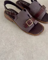 Sandalias negras con suela plana, tira ancha de gamuza con hebilla plateada y tira trasera ajustable.