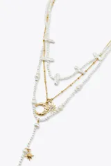 Set de tres collares de diferentes largos. Uno de perlas de diferentes tamaños con cierre de mosquetón. Otro de eslabones metálicos dorados con colgantes en forma de sol y luna. El tercero de perlas de diferentes tamaños con colgantes metálicos dorados en forma de luna labrada y estrella.