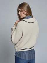 Sweater color crema de tejido grueso con medio cierre, cuello alto y detalles deportivos con rayas negras en puños y hombros.