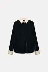 Camisa negra de terciopelo con cuello solapa, manga larga con puños en tejido color crema a contraste y bajo redondeado.
