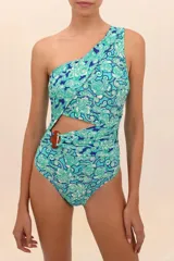 Traje de baño entero con estampado floral en tonos celeste, azul y blanco. Diseño de un hombro con abertura lateral y faja drapeada con accesorio decorativo de piedra color marrón.