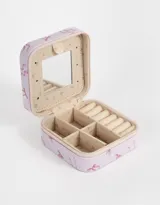 Caja cuadrada porta bijou color lila con estampado de moños rosas y cierre perimetral con cremallera.