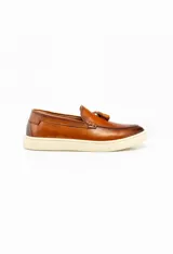 Mocasín de cuero color marrón con suela de goma color crema y detalle de pompón en la capellada.