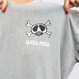 Remera gris de manga corta con cuello redondo y estampado pequeño en el pecho de una calavera con lentes de sol y el texto "La Vela Puerca".