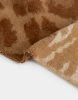 Bufanda rectangular tejida en tonos beige y marrón con estampado animal print y flecos en los extremos.