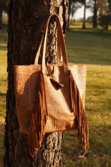 Bolso maxi de cuero marrón con textura croco, flecos laterales y botón de guampa. Tiene bolsillo interior y cierre metálico.