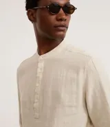 Camisa blanca de manga larga, corte amplio y cuello padre (mandarín). Presenta un frente abotonado con tapeta corta.