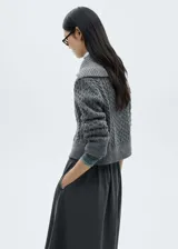 Cárdigan gris de tejido de punto grueso con diseño trenzado, cuello camisero, cierre frontal con botones y terminaciones acanaladas.
