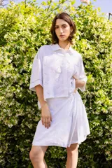 Camisa blanca de lino bordado, corte amplio y largo cropped, con cuello clásico y bolsillo frontal.