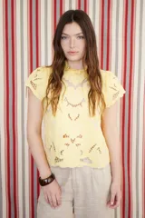 Blusa amarilla de algodón con bordado calado (broderie) en el frente y mangas cortas. Presenta cuello alto con detalle de lazo o moño.
