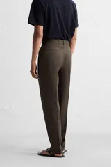 Pantalón de vestir color marrón oscuro, confeccionado en lino italiano. Presenta corte regular fit, cintura con pliegues, bolsillos laterales y traseros ribeteados, y terminación con dobladillo. Cierre frontal con cremallera y botón.
