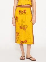 Pollera midi amarilla con estampado de broderie y arte exclusivo de JCH. Presenta tiras color caramelo en cintura y laterales. De calce al cuerpo, incluye cierre metálico lateral a tono con la base.