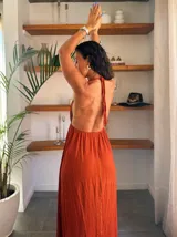 Vestido largo blanco con finas rayas verticales en lurex dorado. Presenta un escote profundo en V con tirantes finos que se anudan en la nuca (estilo halter) y un corte imperio con frunces en la cintura.