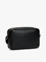 Cartera tipo cámara cruzada (crossbody) color negro, con acabado liso y logo metalizado de Tommy Hilfiger en el frente. Posee un compartimento principal con cierre de cremallera y un asa tejida ajustable.