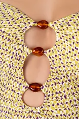 Traje de baño entero con estampado de lunares amarillos y violetas, con escote bandeau y breteles semi-amplios. Presenta cortes circulares con cuentas marrones en el centro y recogidos laterales. Breteles ajustables en la espalda.