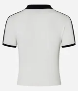 Blusa polo de malla de algodón color blanco con cuello y mangas cortas con ribete negro. Presenta bordado de moña en el pecho y dos rayas negras en cada manga.