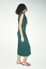 Vestido midi verde oscuro de cuello redondo y sisa americana. Presenta un drapeado en el lateral con detalle de hebilla metálica y abertura en la falda.