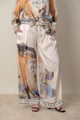 Pantalón palazzo italiano de satén de seda color natural con estampado en tonos de verde, lila y naranja. Cintura con elástico y cordón, bolsillos laterales. Cintura y bajo con guarda escrita.